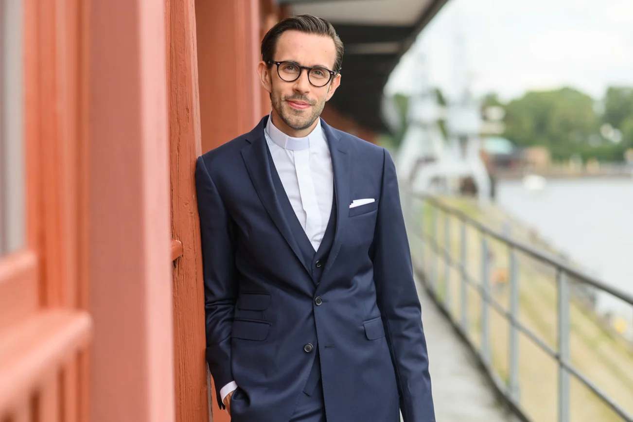 Ein Mann steht an einer Hauswand und blickt in die Kamera. 