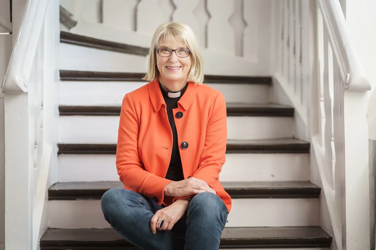 Proepstin Frauke Eibensitzt auf der unteren Stufe einer weißen Holztreppe mit braunen Stufen.