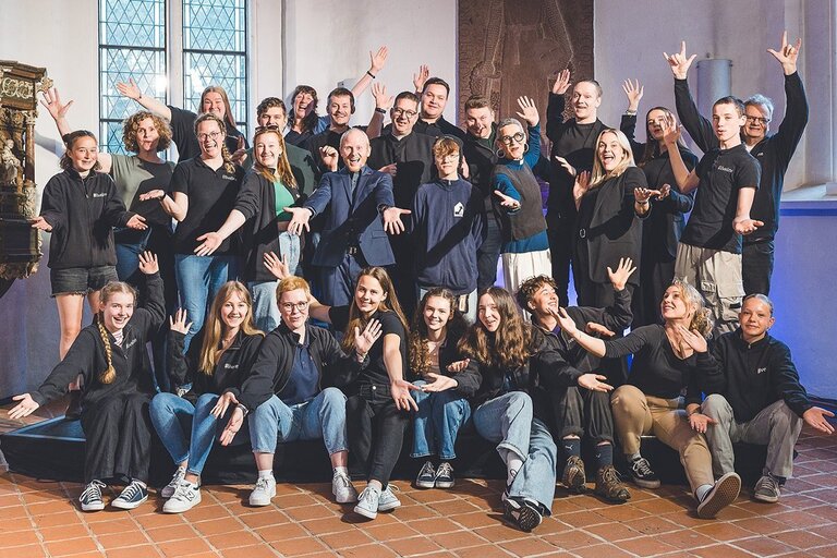 Eine Gruppe von Menschen stehen und sitzen hintereinander, einige haben die Arme hochgestreckt